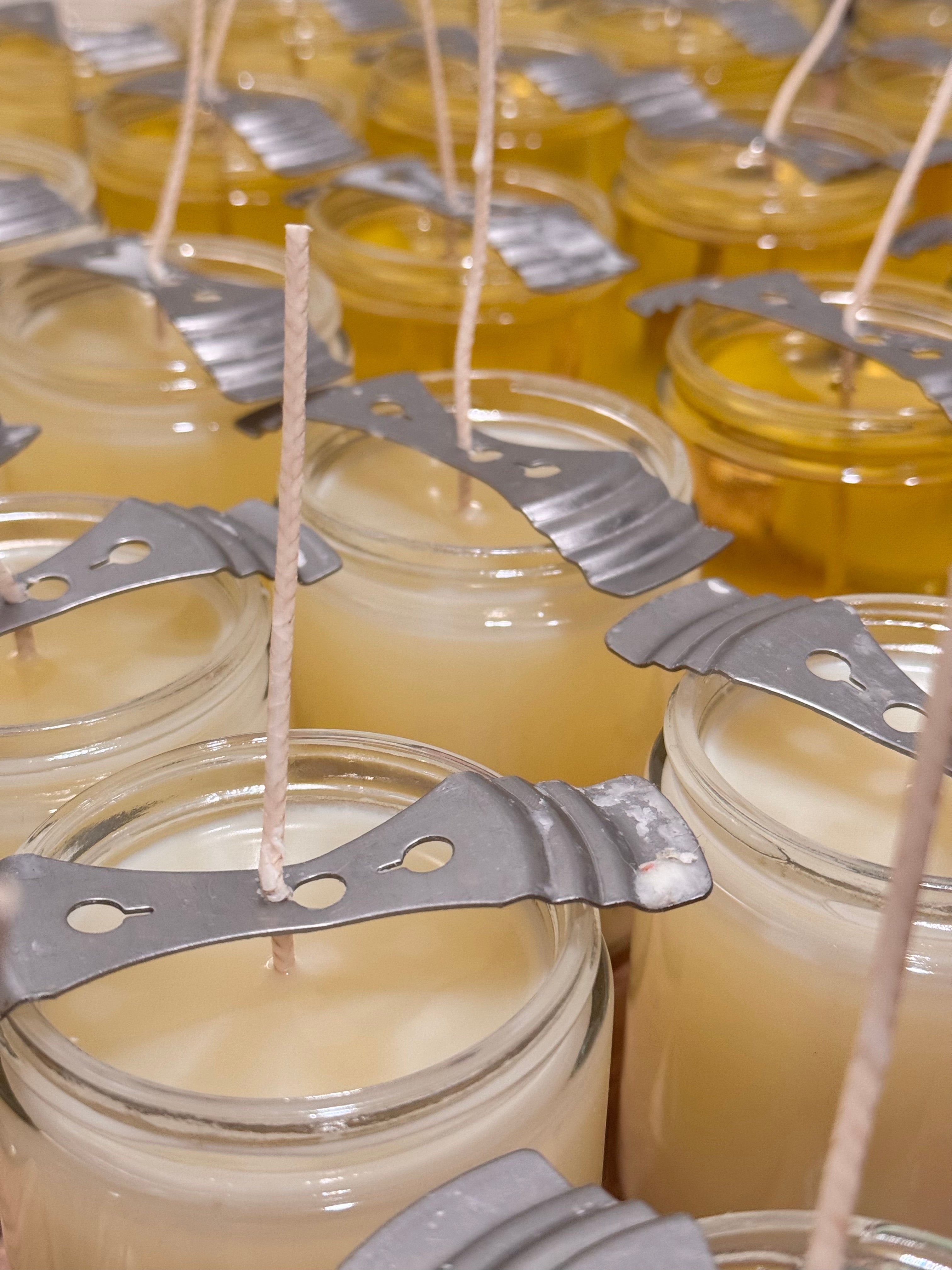 several glass jars filled with a yellow liquid, likely wax, and metal skewers or wicks inserted into them.